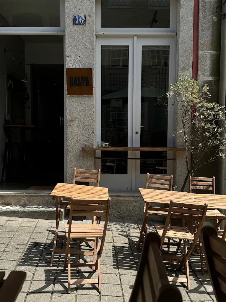 Balta's entrance in the sun, with the BALTA sign and tables on the terrace